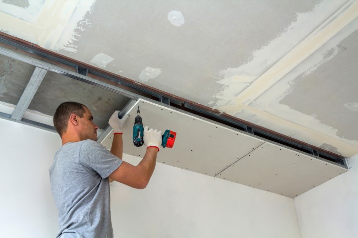 Construction Worker Assemble A Suspended Ceiling With Drywall An